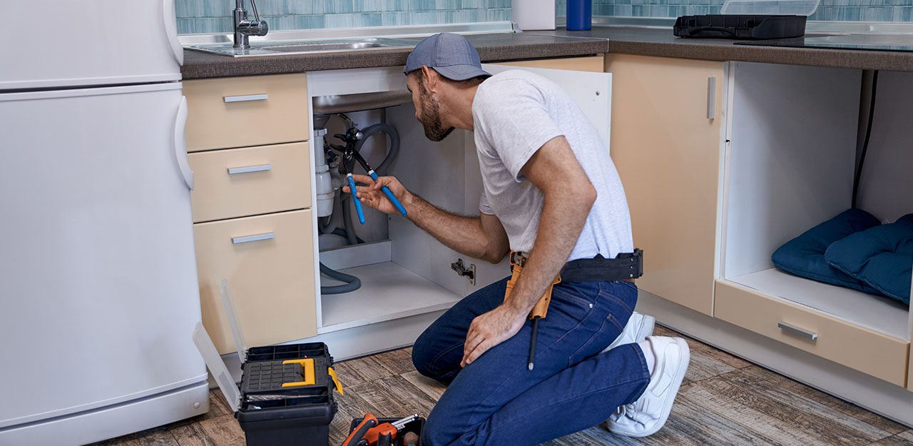 Técnico joven reparando tuberías bajo el fregadero en una cocina residencial.